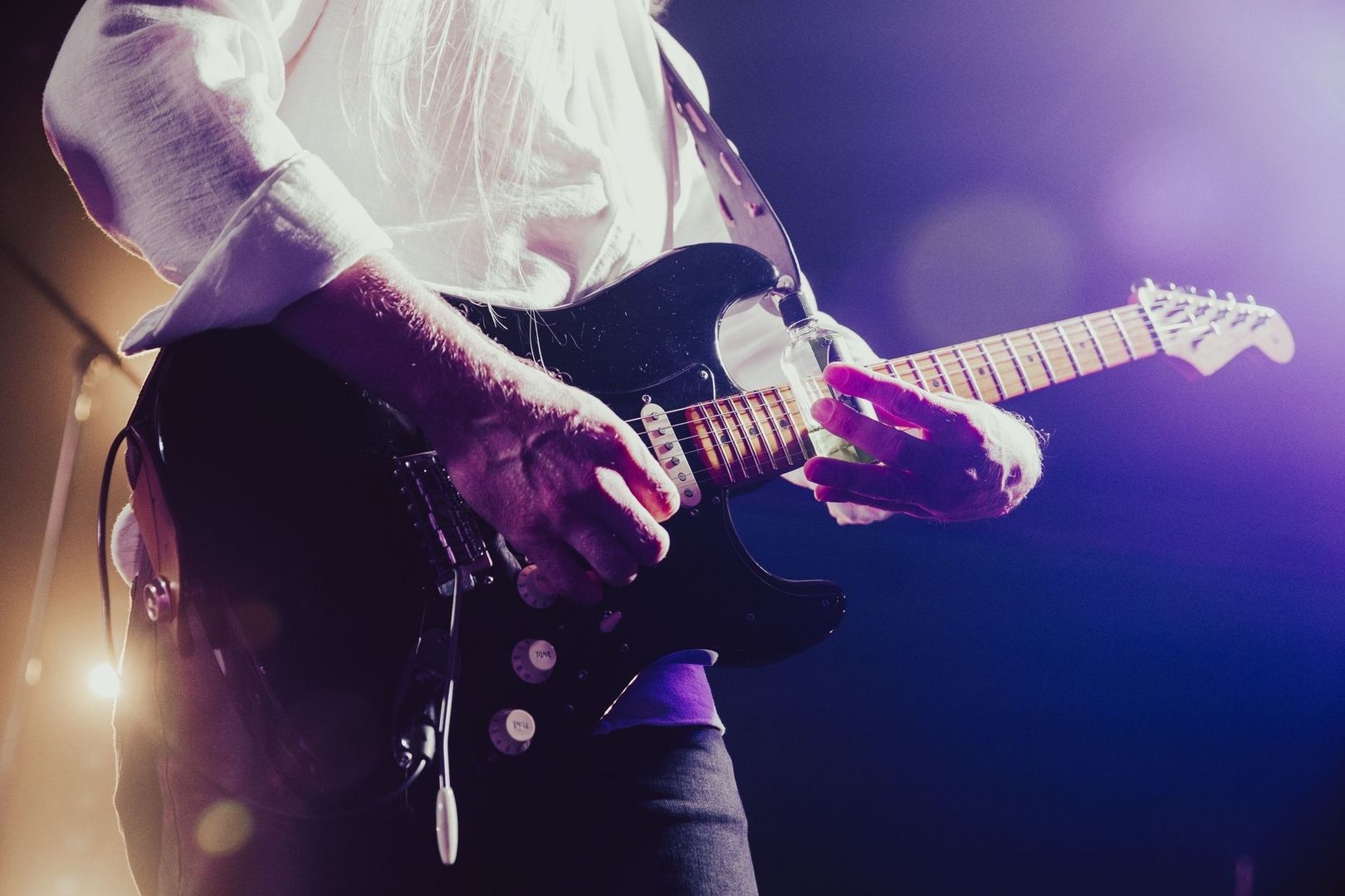 Nahaufnahme eines Gitarristen mit schwarzer E-Gitarre im violetten Bühnenlicht